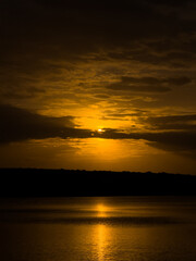 Dramatic golden sunset with glowing clouds and sun reflection on calm water, creating a peaceful and atmospheric evening landscape view.