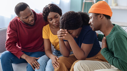 Supportive black friends consoling their crying girlfriend, hugging her and saying good words, home interior. Sad african american lady sharing her problems with friends. Friendship, support concept