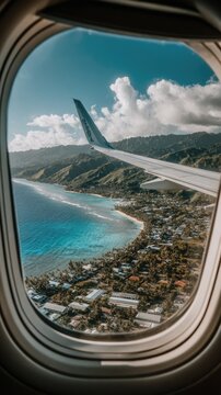 Fototapeta High-angle view of a tropical coastal landscape seen from an airplane window, showcasing vibrant turquoise water, lush green hills, and a collection of buildings along the shore.