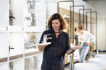 Male buyer compares black and gray stainless steel water faucets. supermarket of building materials and repair goods