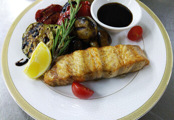 Baked sturgeon steaks with fresh salad greens, basil leaves and cherry tomatoes on a large white plate. delicious and healthy food for kids and adults. diet food. grilled vegetables next to the fish