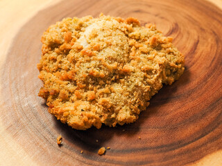 Breaded chicken breast fillet on a wooden board. Classic poultry product. Uncooked meat covered with golden breadcrumbs.