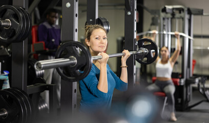Caucasian woman training with barbell using squat rack in gym
