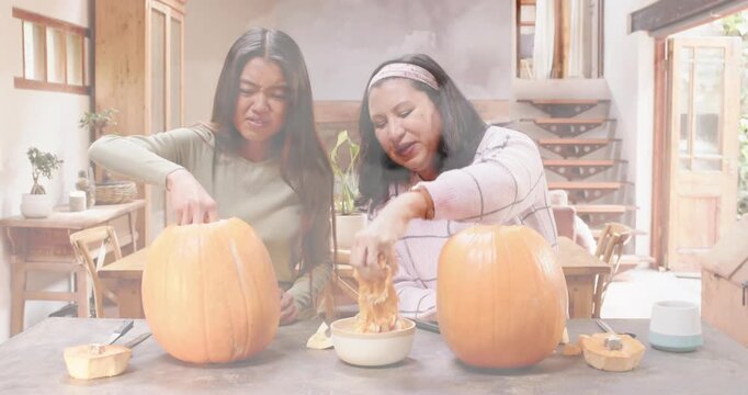Two friends plunging hands into pumpkins in DIY workshop, extracting pulp into bowl for carving