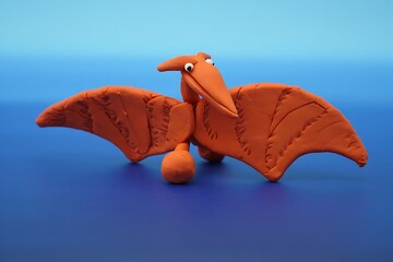 Orange Clay Pterodactyl Dinosaur with Googly Eyes on a Blue Background
