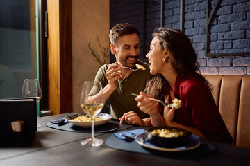 Happy man feeding his girlfriend during their lunch in a restaurant.