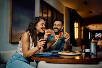 Young happy couple eating pizza while being on a date in pizzeria.