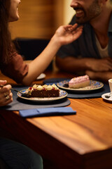 Close up of couple eating cake while dating in cafe.