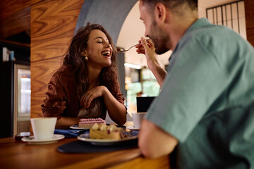 Happy woman tasting boyfriend's cake during their date in cafe.