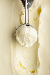Vanilla ice cream scoop in metal spoon over creamy background, macro food texture shot