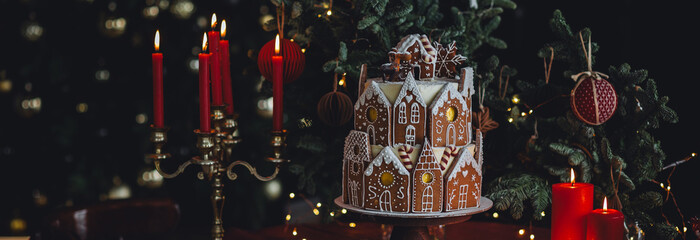 Family holiday celebration. Beautiful traditional homemade gingerbread house. Celebration of Christmas and Happy new year at home. Festive mood, cozy atmosphere, burning candles, fir tree. Banner