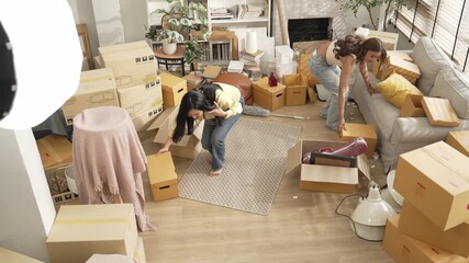 Lesbian lover placing box at living room floor and dancing together. Attractive friend working together and moving to a new house while moving to music at room surrounded with cardboard box. Myrmidon.