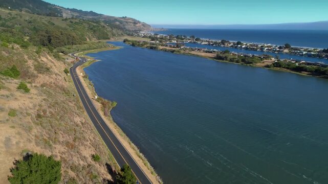 Aerial view of a car driving along Highway 1 next to the Bolinas Logoon, Stinson Beach, California, USA. The road winds along the river, with mountains in the background.