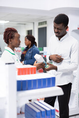 Fototapeta premium African american expert offers medication for a guy with abdominal pain, assisting client in treating a digestive inflammation or food poisoning. Pharmaceutical care in a retail setting.