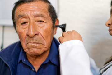 Doctor examining senior man's ear with otoscope in medical checkup