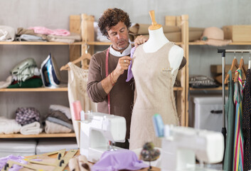Adult male tailor adjusting clothes on mannequin in sewing workshop
