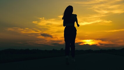 Obraz premium Chasing sun. Training jogging. Running outside city, girl runner breathing in fresh air. Beautiful girl doing fitness, jogging on road in sun. Young woman legs running on asphalt at sunset, Silhouette