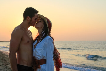 Fototapeta premium Happy young couple tenderly embracing and kissing at the beach at sunset.