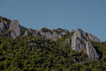 Rocky mountain landscape in the Caucasus region. Steep cliffs rise above lush green vegetation under a clear blue sky.