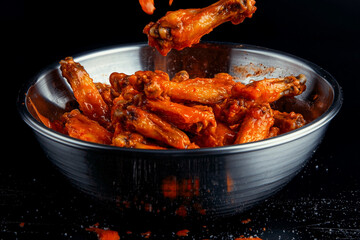 Buffalo chicken wings fall into a bowl - isolated,  black background - spicy hot wings with sauce tossed after being fried, slow motion closeup - hot wings