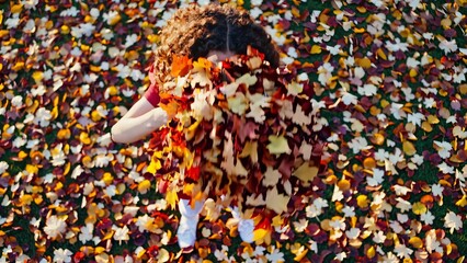 Fototapeta premium A person is surrounded by falling autumn leaves, creating a colorful and dynamic scene.