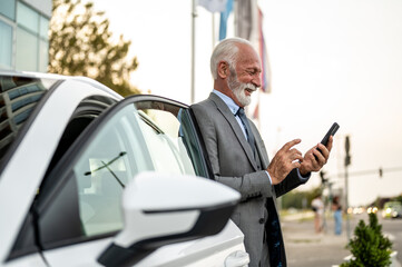 Senior businessman using smartphone near car in city