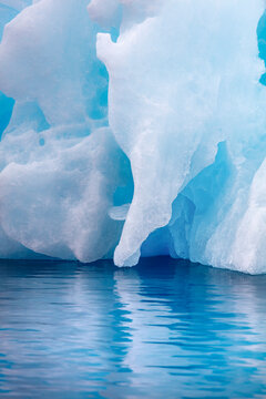 Close-up of a blue iceberg reflected in calm Antarctic waters. The intricate textures and colors of the ice reveal the beauty and fragility of polar environments.