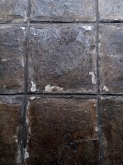 A close-up of a floor paved with large, dark gray and brown square tiles, showing weathering and wear.