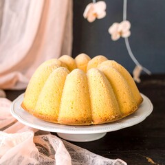 Light yellow bundt cake on a white stand, soft pink backdrop
