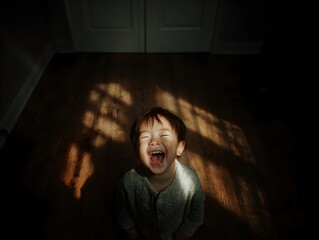 A joyful young boy laughs gleefully in a dark room illuminated by patterned sunlight on his face and body.