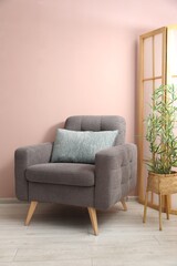 Comfortable armchair with cushion and houseplant near beige wall indoors