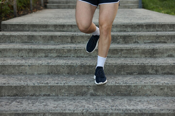 Athletic young man in sportswear running down stairs outdoors, closeup