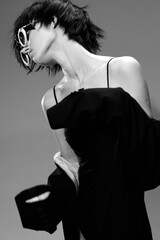 Black and white portrait of a fashion woman with short hair wearing sunglasses and stylish dress in studio lighting.