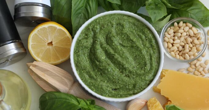 Fresh pesto sauce in bowl, ingredients and squeezer on white marble table, flat lay