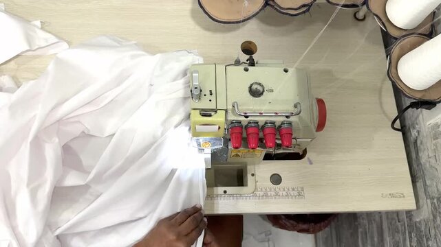 Skilled seamstress expertly guides white fabric through an industrial overlock sewing machine, creating precise seams
