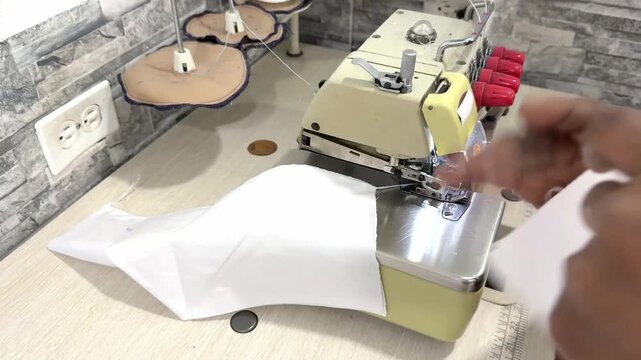 Close-up of a seamstress using an overlock sewing machine on white fabric
