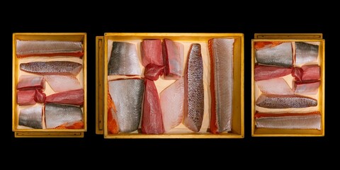 Top view of assorted fresh raw fish fillets in a wooden box.
