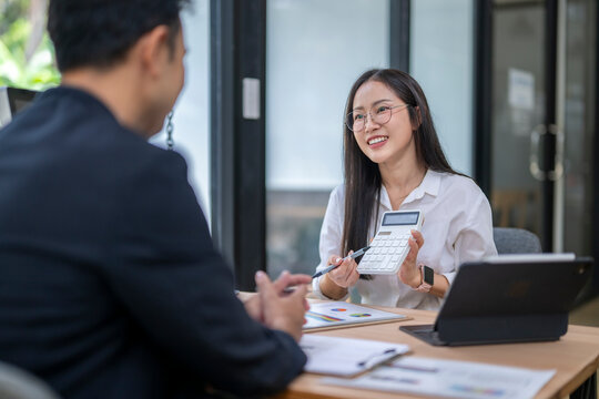 Asian businesswoman showing calculator to businessman during meeting - Powered by Adobe