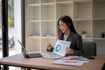 Asian businesswoman presenting financial data on video call using laptop and charts