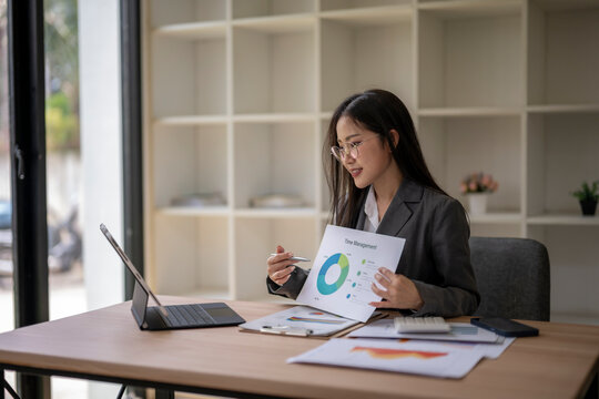 Asian businesswoman presenting financial data on video call using laptop and charts