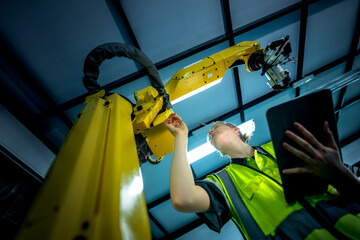 A female maintenance technician performs a preventative maintenance check on a 6-axis robotic arm's end-effector, ensuring the system's precision on the production line.