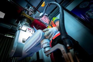 A team of diverse engineers in safety gear performs a maintenance inspection on an industrial robot. They are working together to solve a technical issue in the factory.