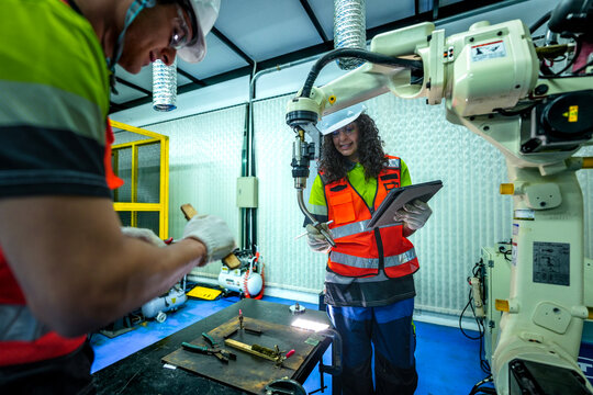 A team of diverse engineers in safety gear performs a maintenance inspection on an industrial robot. They are working together to solve a technical issue in the factory.