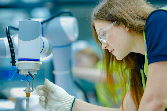A female technician attaches a pneumatic end-effector to a 6-axis collaborative robot (cobot). She is setting up the robotic cell for a precise, automated assembly task.