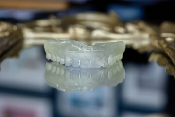 Transparent 3D printed dental model placed on a decorative reflective surface. Concept of digital dentistry, orthodontic planning, and modern dental prosthetics.