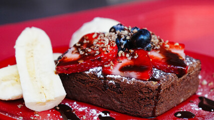 Brownie con helado y plátano servido en plato rojo
