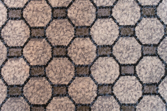 Textured carpet surface with repeating octagonal pattern in shades of grey and blue, forming a geometric grid design.