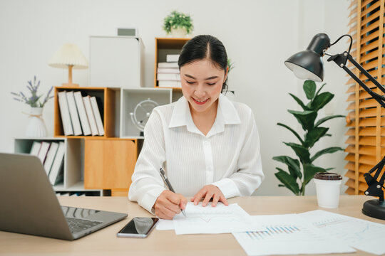 happy woman writing cocument or paperwork with laptop at home office