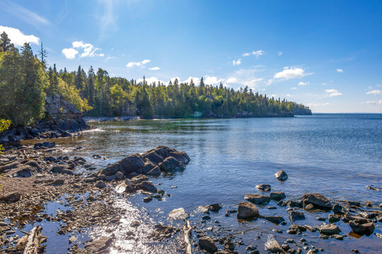 Tranquil view of Sleeping Giant Provincial Park's serene shoreline, showcasing rocky outcrops and lush boreal forest under a clear blue sky. - Powered by Adobe