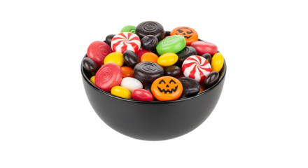 Assorted candies in a black bowl, including pumpkin shaped sweets and peppermint swirls on a surface